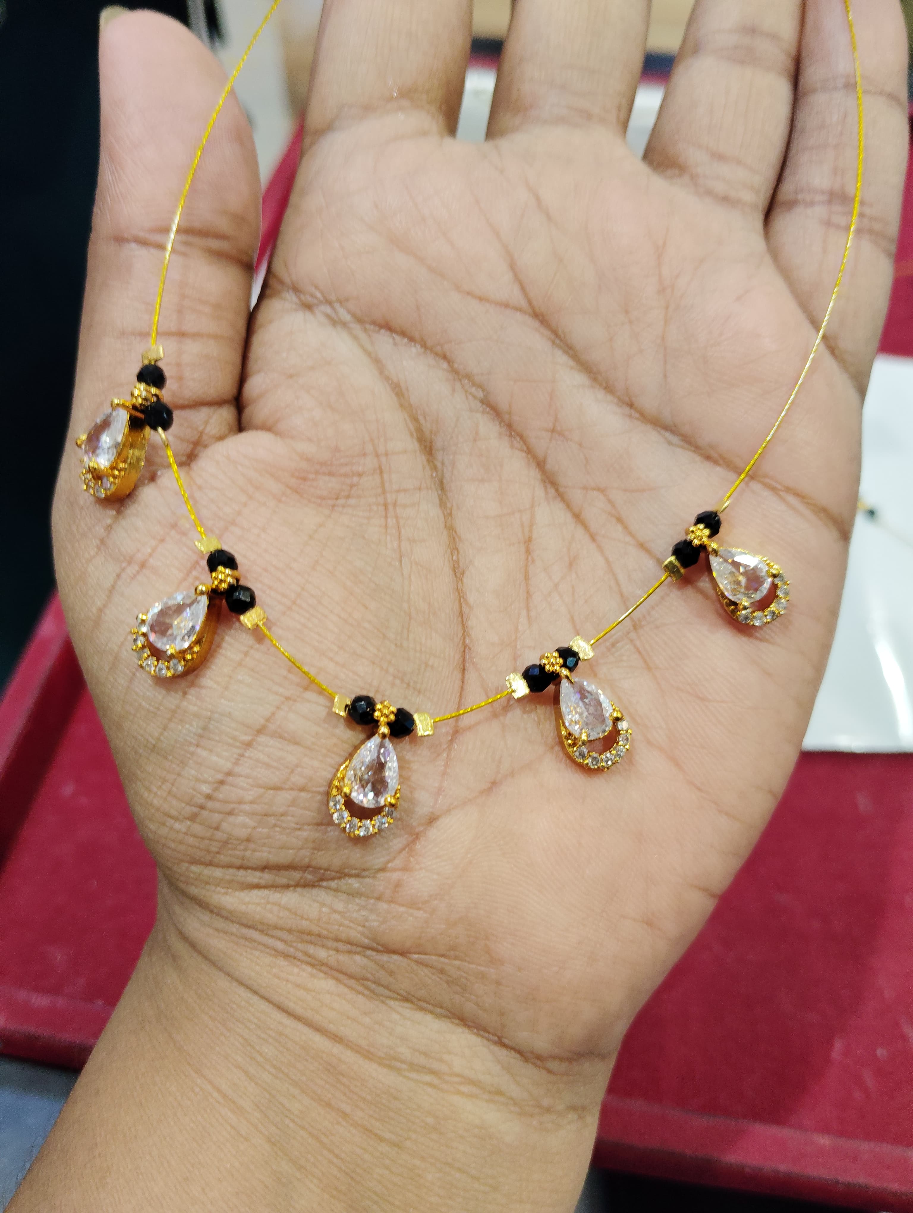 Fine mangalsutra with black beads and teardrop clear crystal charms on a gold-coloured thread